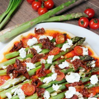 Pizza mit grünem Spargel, Tomaten und Feta auf dem Teller