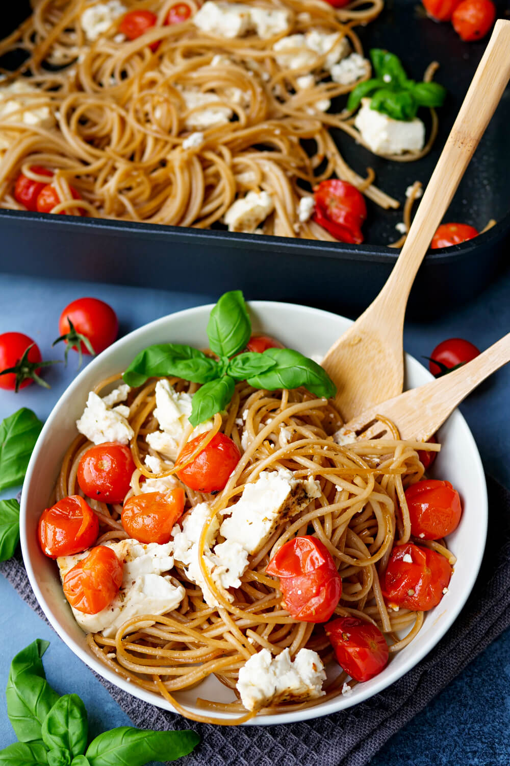 Feta Pasta mit Tomaten und Basilikum in der weißen Schüssel mit Auflaufform im Hintergrund
