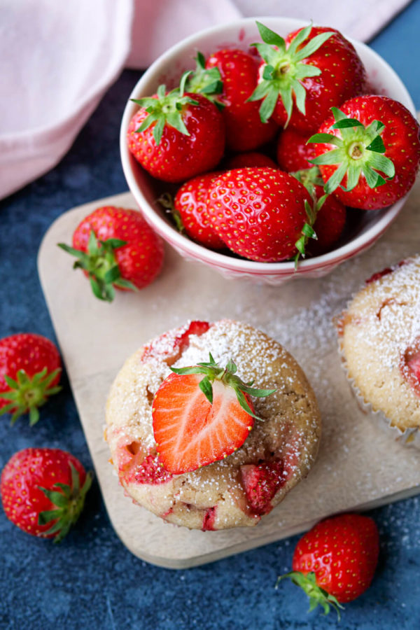 Erdbeer-Vanille-Muffins mit Puderzucker und halbierten Erdbeeren auf dem Holzbrett