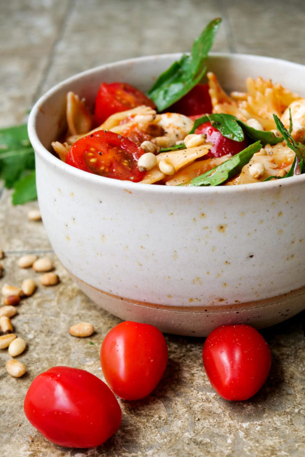 Italienischer Nudelsalat mit Pinienkernen, Mozzarella, Rucola und Tomaten in der Schüssel
