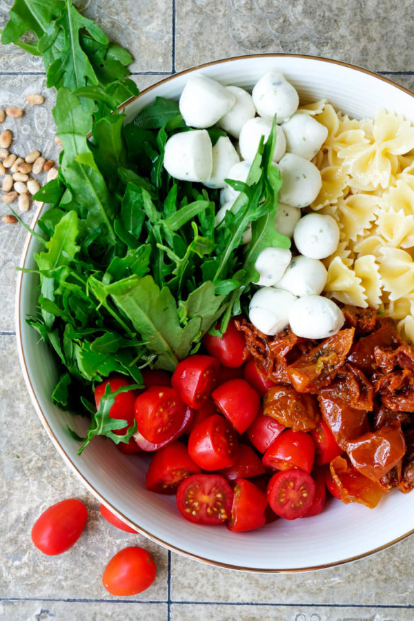Rucola, Tomaten, Mozzarella, getrocknete Tomaten und Nudeln sind die Zutaten für den italienischen Nudelsalat
