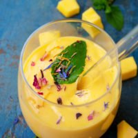 Mango Lassi mit frischer Minze und essbaren Blüten im Glas