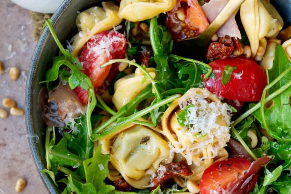 Tortellinisalat Rezept mit Parmesan, getrockneten Tomaten, Schinken, Rucola und Pinienkernen
