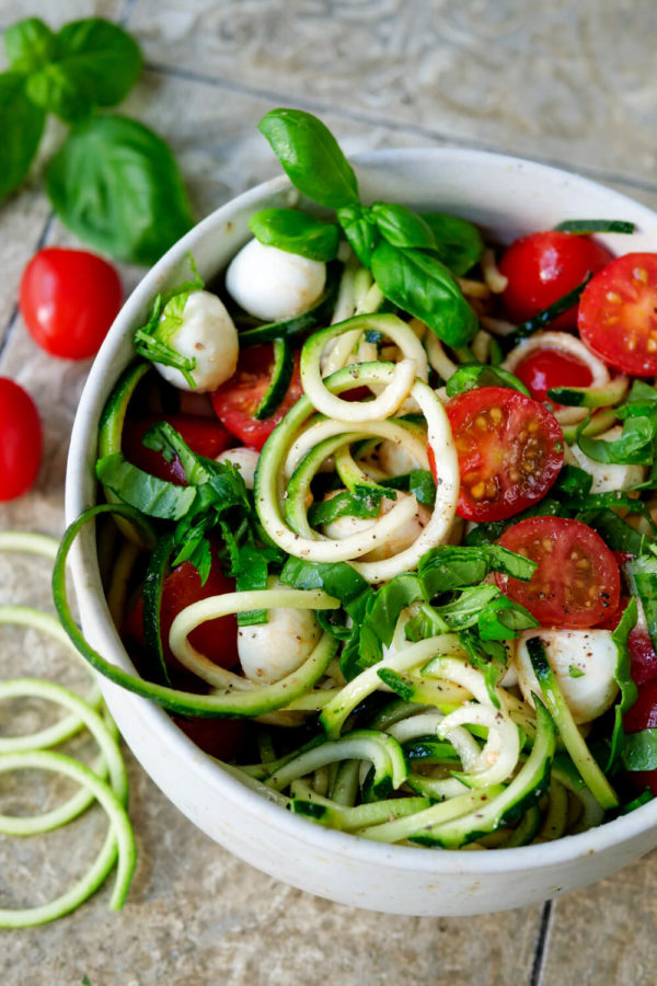 Roher Zucchini-Salat mit Tomaten, Mozzarella und Basilikum in der Schüssel
