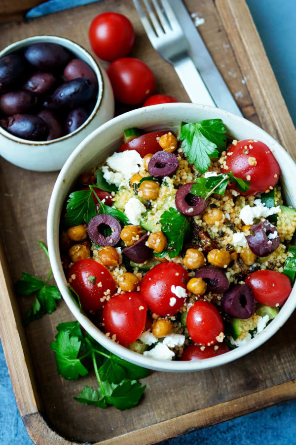 Kichererbsen-Couscous-Salat mit Oliven und Tomaten auf dem Holz-Tablett