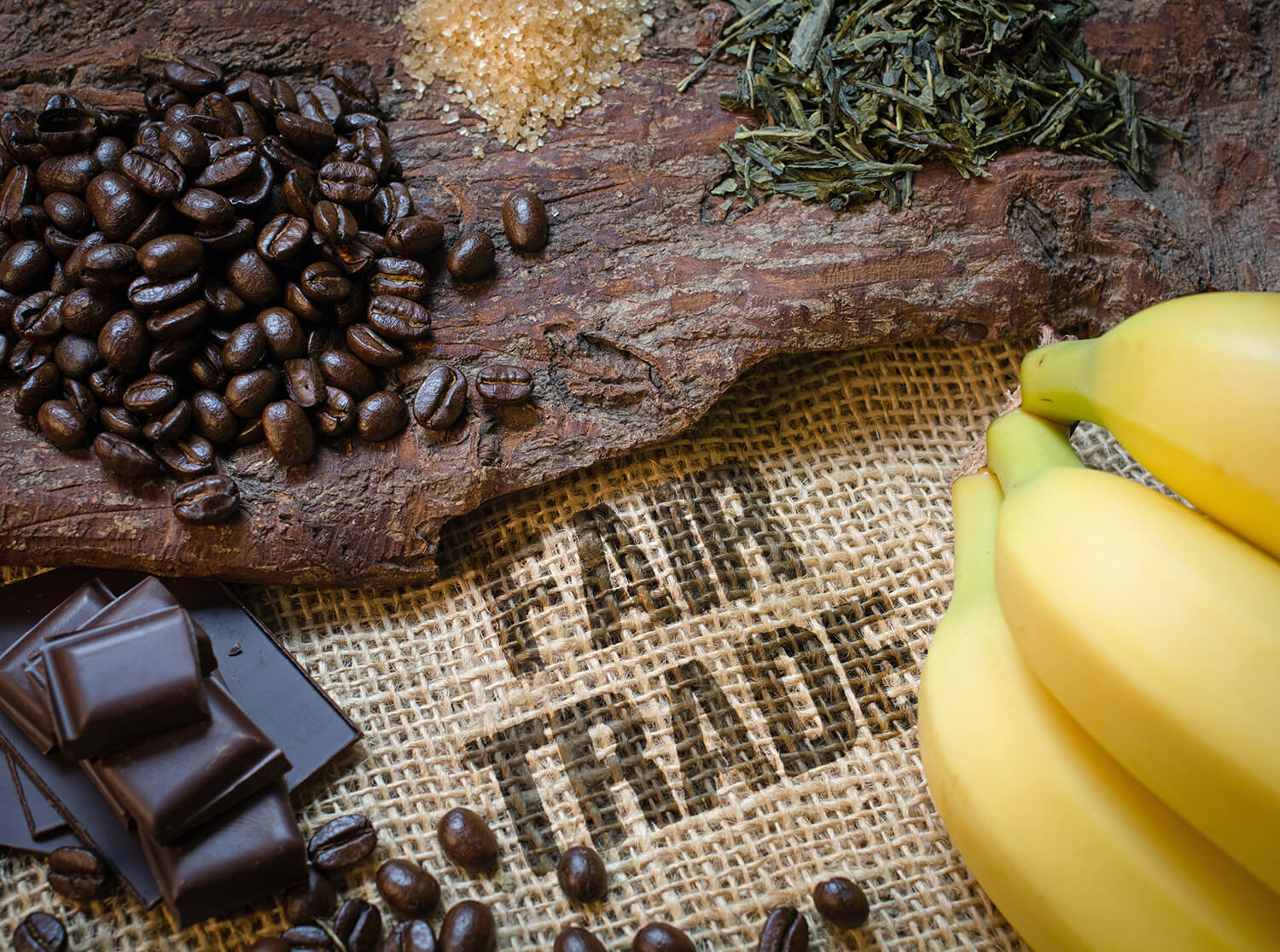 Kaffeebohnen, Schokoladenstück und Bananen auf Untergrund mit Fairtrade-Stempel