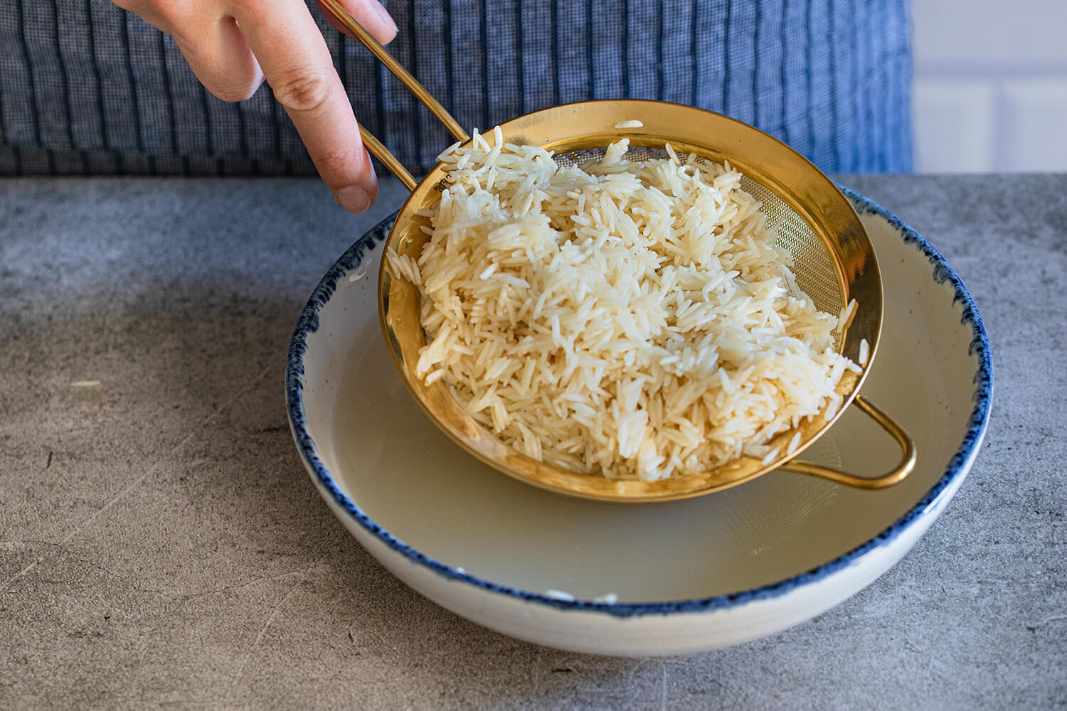 Gewaschener Reis tropft aus Sieb in Teller ab