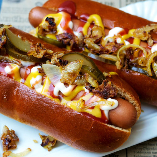 Hotdog mit Würstchen, Ketchup, Senf, Remoulade, Gurken und Röstzwiebeln