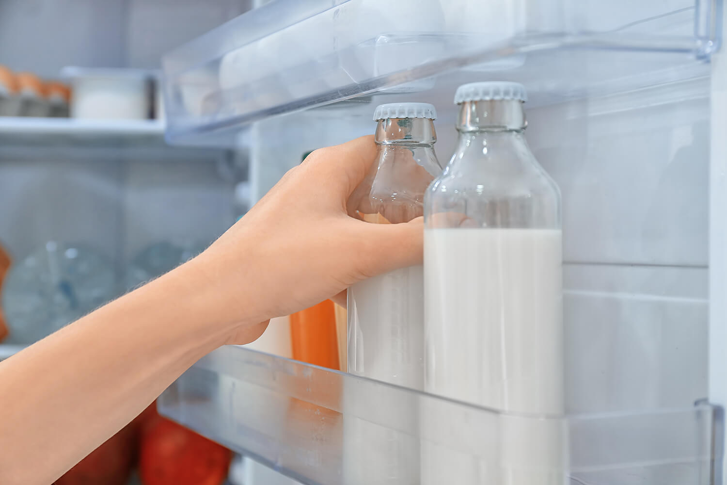 Hand greift zu einer von zwei Milchflaschen in der Innentür eines Kühlschranks