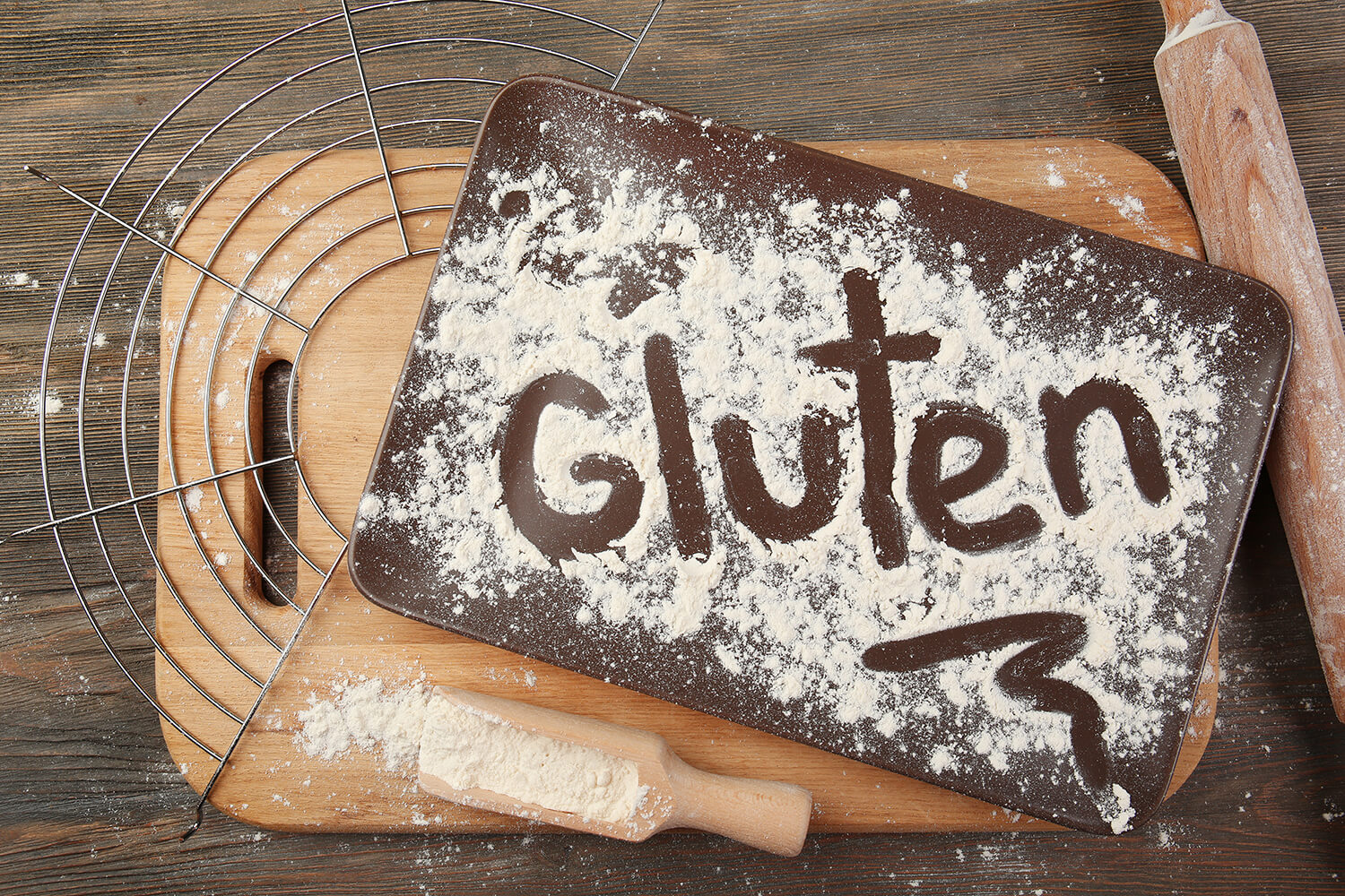 Das Wort Gluten mit Mehl auf einem Tablett über Holztisch geschrieben