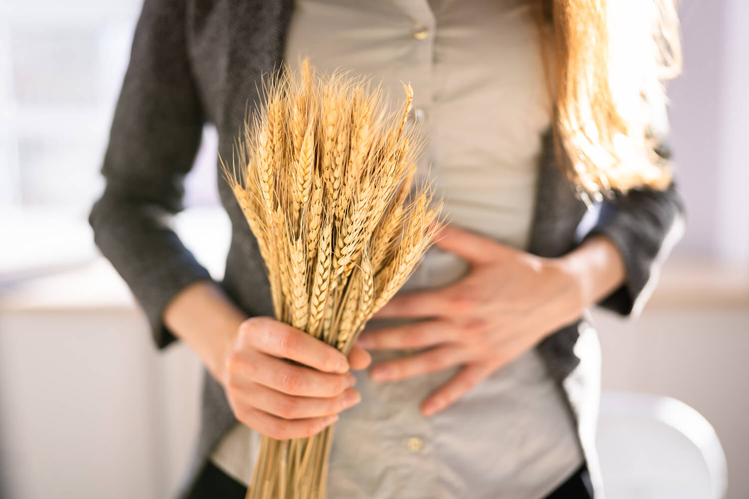 Frau mit Weizenähren in der Hand hält sich mit der andern Hand den Bauch