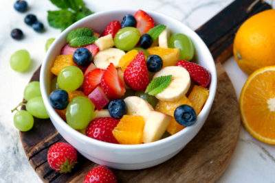 Obstsalat mit Orangen, Weintrauben, Erdbeeren, Banane, Heidelbeeren und Apfel in der Schüssel