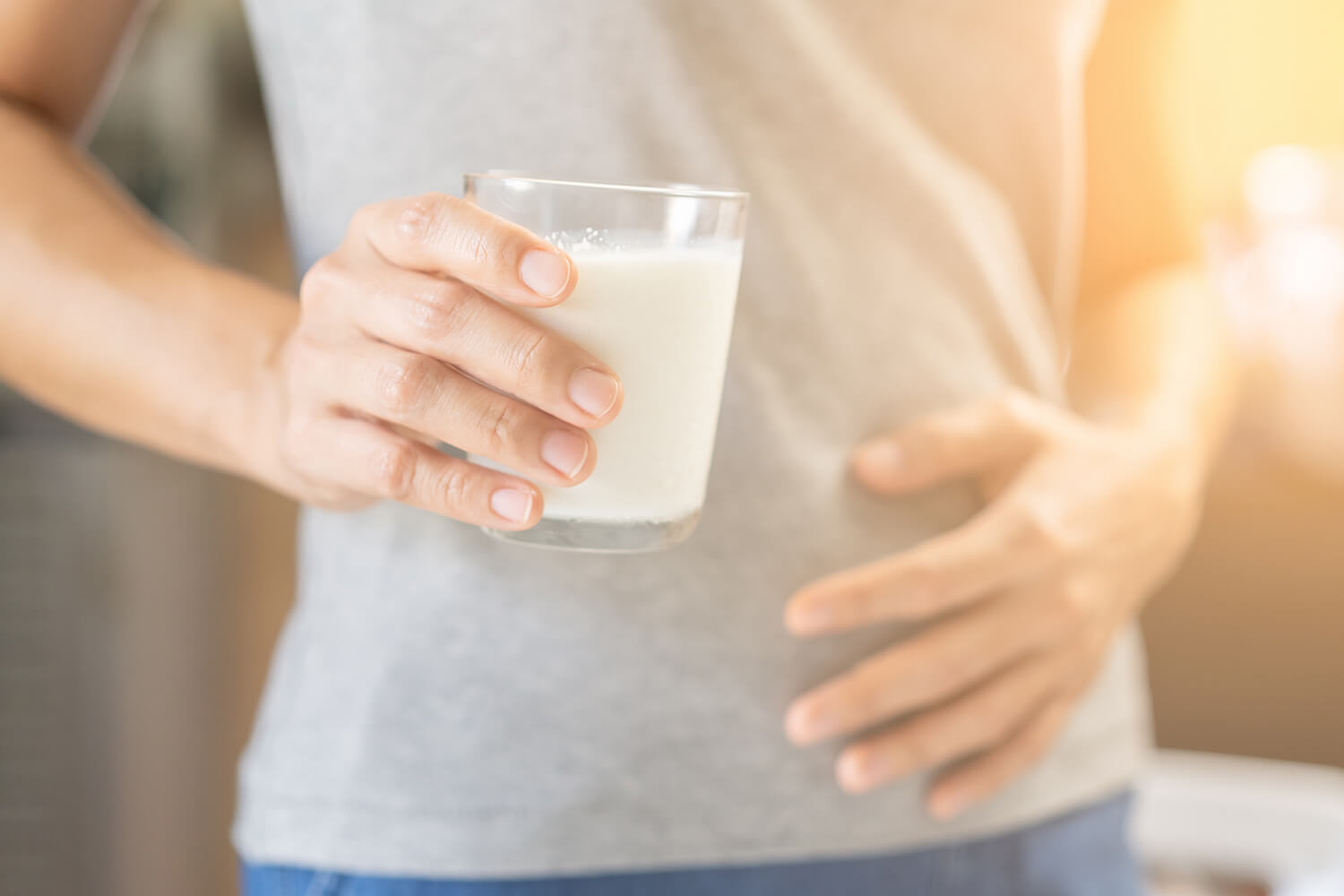 Frau mit Milchglas in der Hand hält sich den Bauch vor Schmerzen