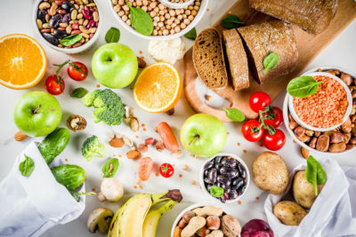 Ballaststoffreiche Lebensmittel – Obst, Gemüse, Kartoffeln, Vollkornbrot – auf weißem Untergrund