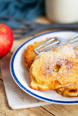Apfelringe im Pfannekuchenteig gebacken und mit Puderzucker bestreut auf dem Teller