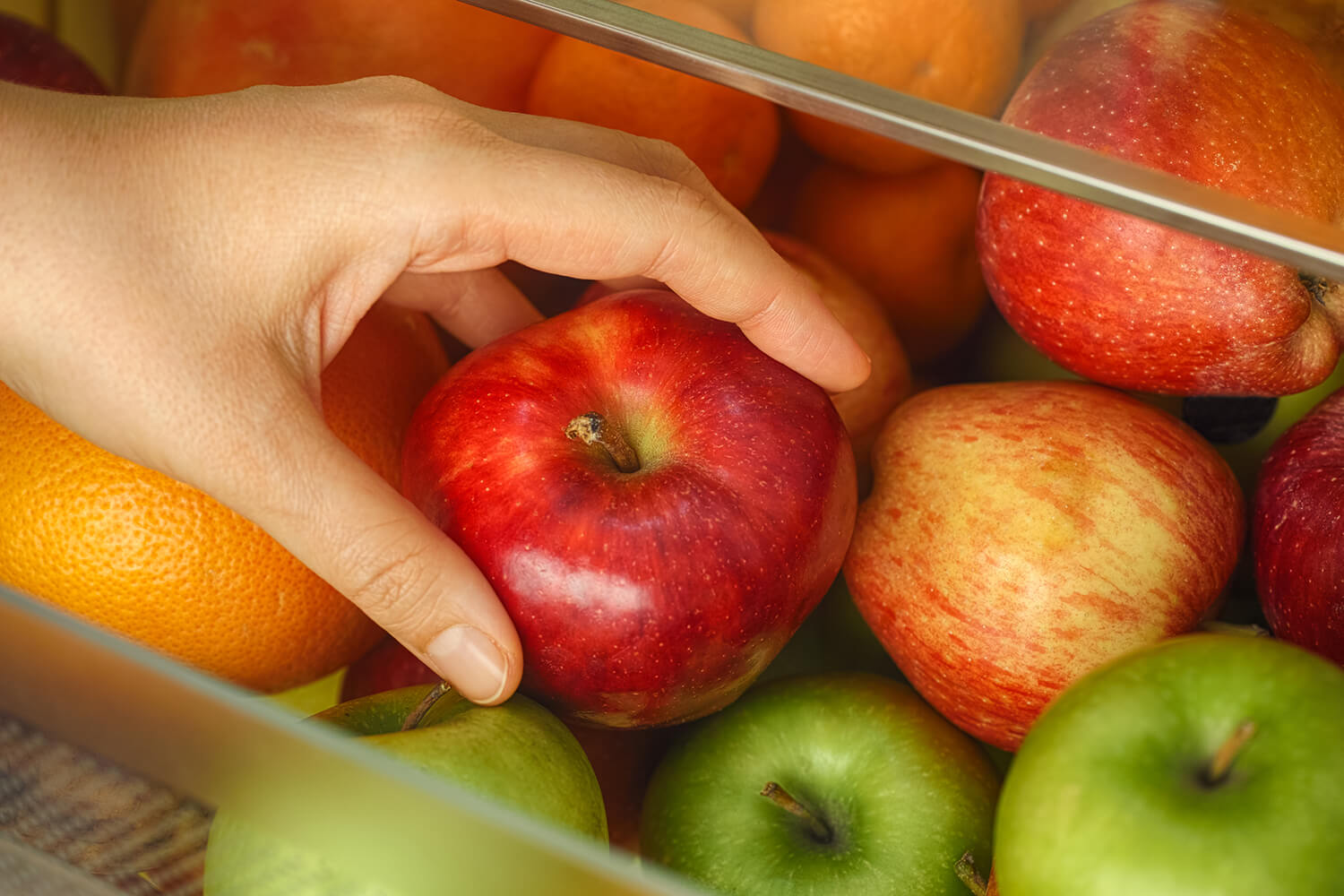 Frauenhand nimmt einen roten Apfel aus Kühlschrank.