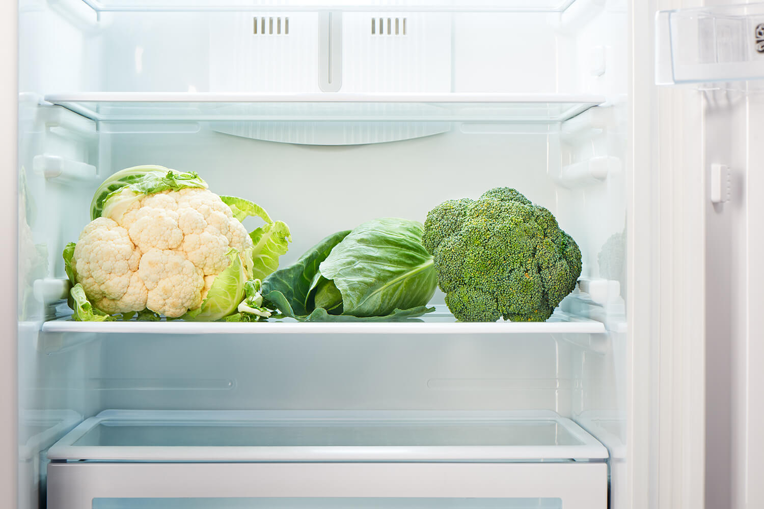 Blumenkohl und weiteres grünes Gemüse liegen im geöffneten Kühlschrank