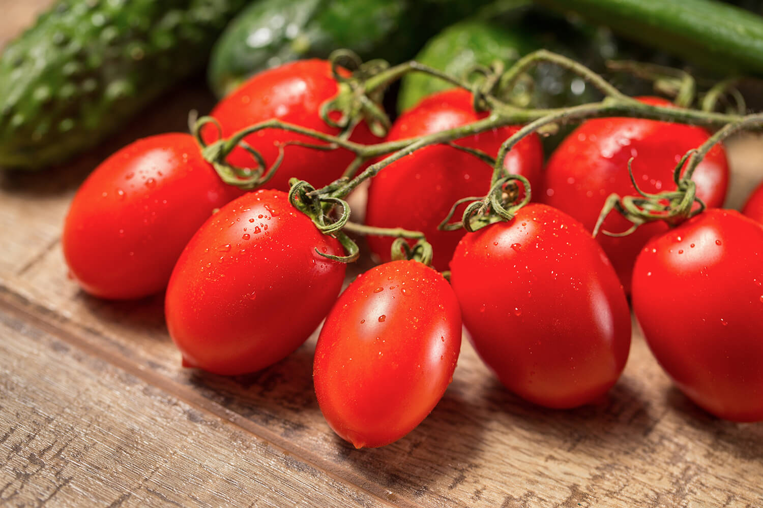 Pflaumen-Roma-Tomaten auf einem Holztisch mit Gurken im Hintergrund