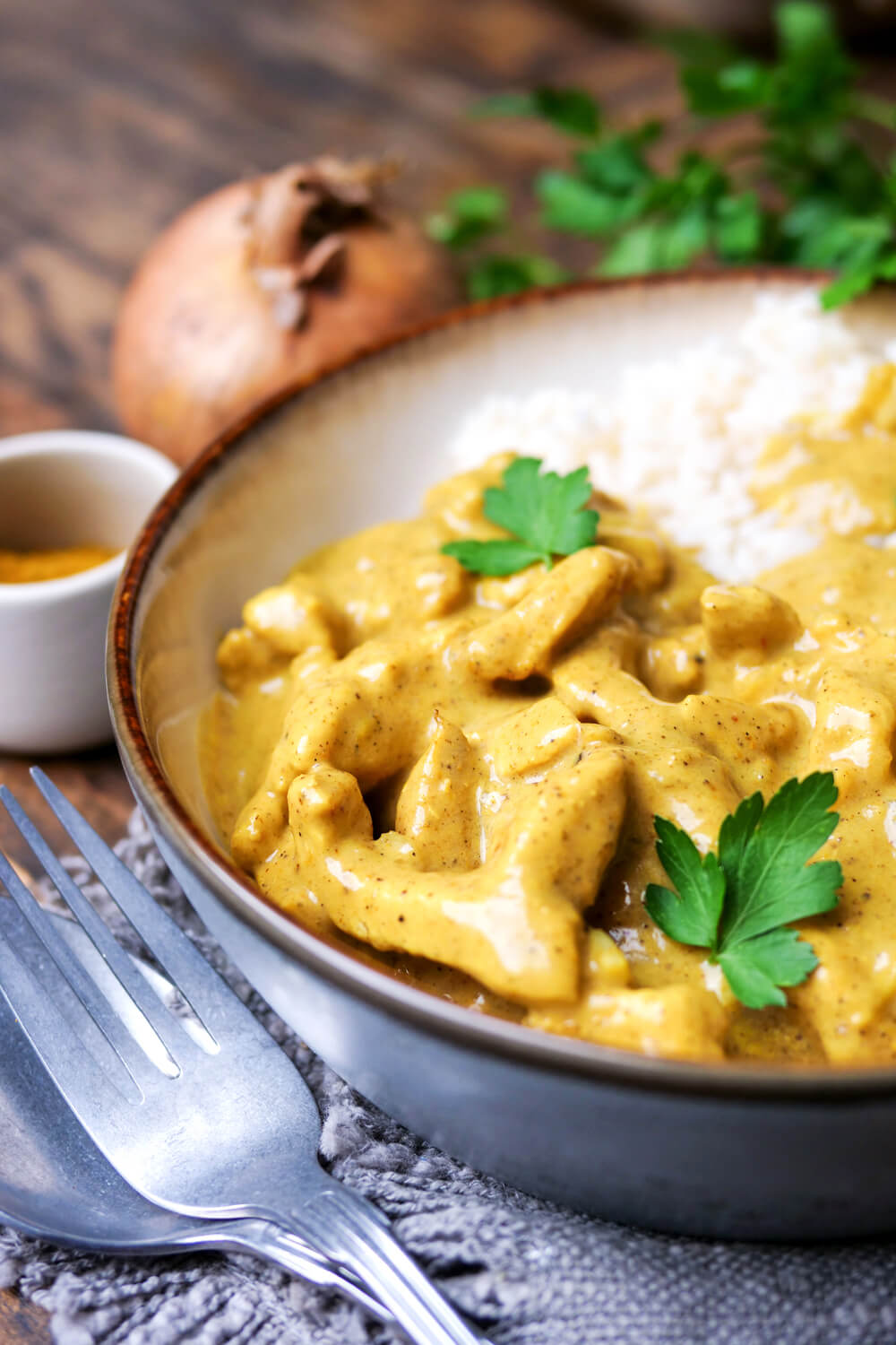 Curry-Geschnetzeltes mit Reis auf einem Teller angerichtet mit angelegtem Besteckt.