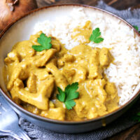 Curry-Geschnetzeltes mit Reis und Petersilie auf einem Teller angerichtet.