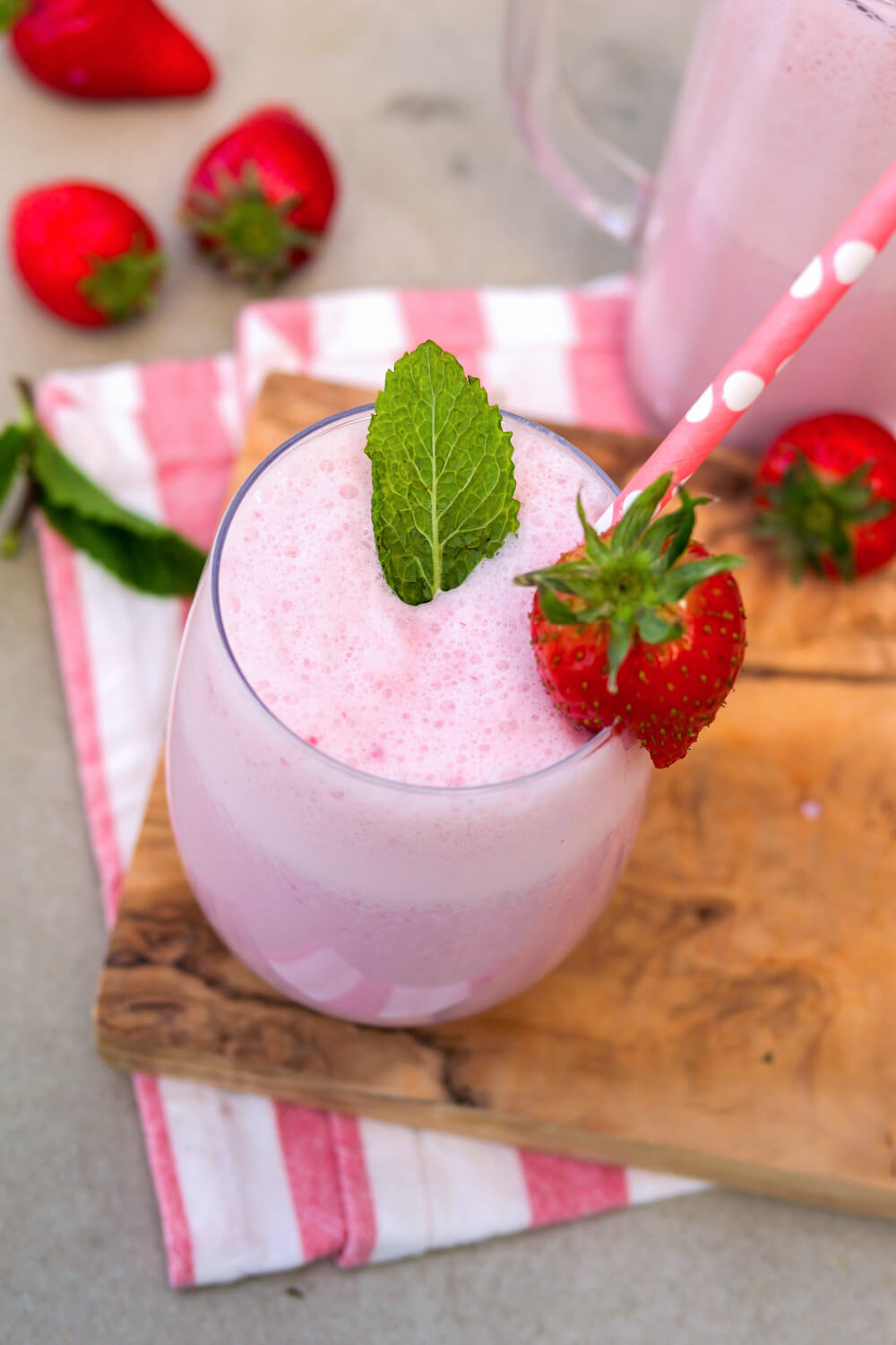 Erdbeer-Milchshake mit Minzblättchen, Erdbeere und Strohhalm in einem Glas auf einem Holzbrett.