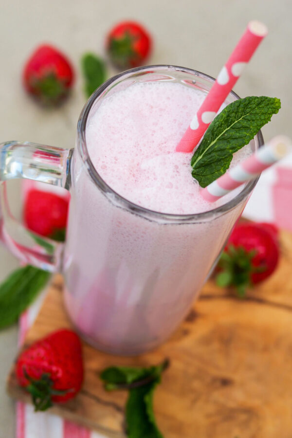 Erdbeer-Milchshake mit Minzblättchen und Strohhalm in einem Glas.
