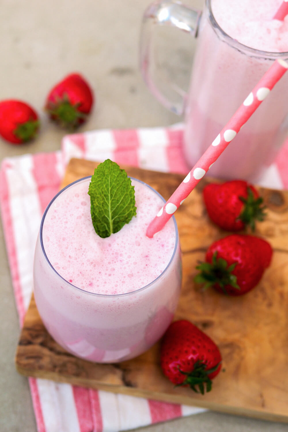 Erdbeer-Milchshake mit Minzblättchen und Strohhalm in einem Glas auf einem Holzbrett.