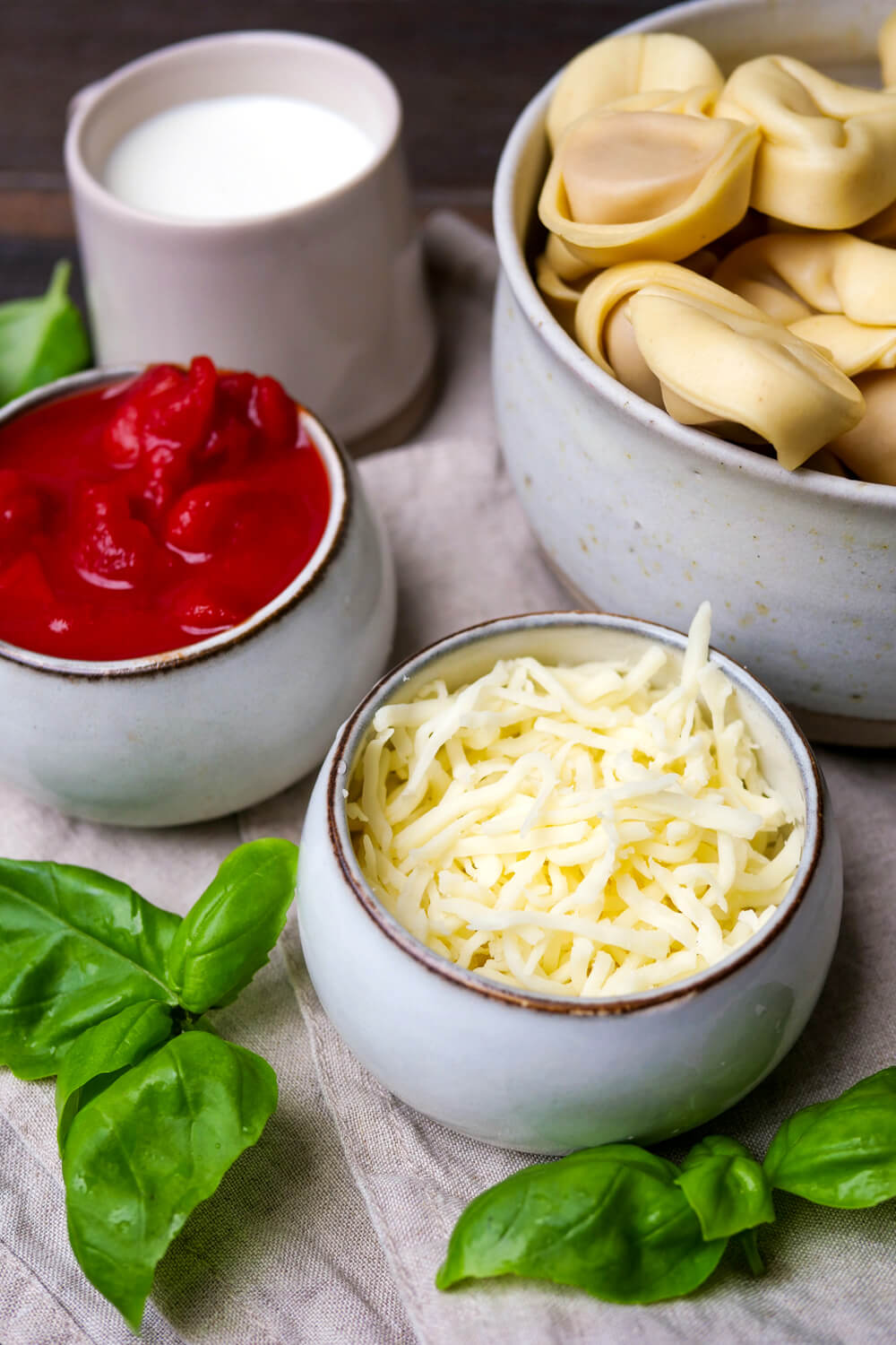 Geriebener Käse, gehackte Tomaten, Tortellini und Sahne in Schalen für Tortellini al Forno.