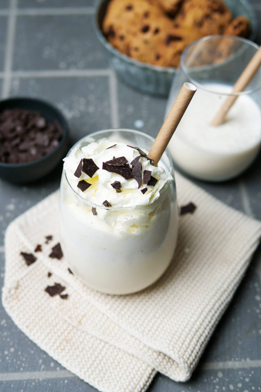 Vanille-Milchshake mit Schokosplitter, Sahne und Strohhalm in einem Glas.