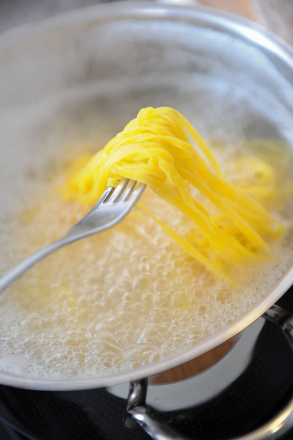Spaghetti auf einer Gabel über einem Topf mit kochendem Wasser.